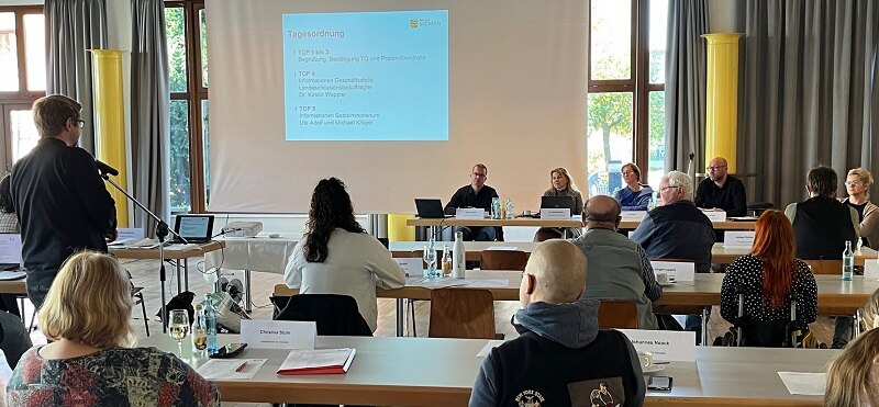 Blick auf Podium und ein Mann im Publikum stellt eine Fragen von hinten zu sehen